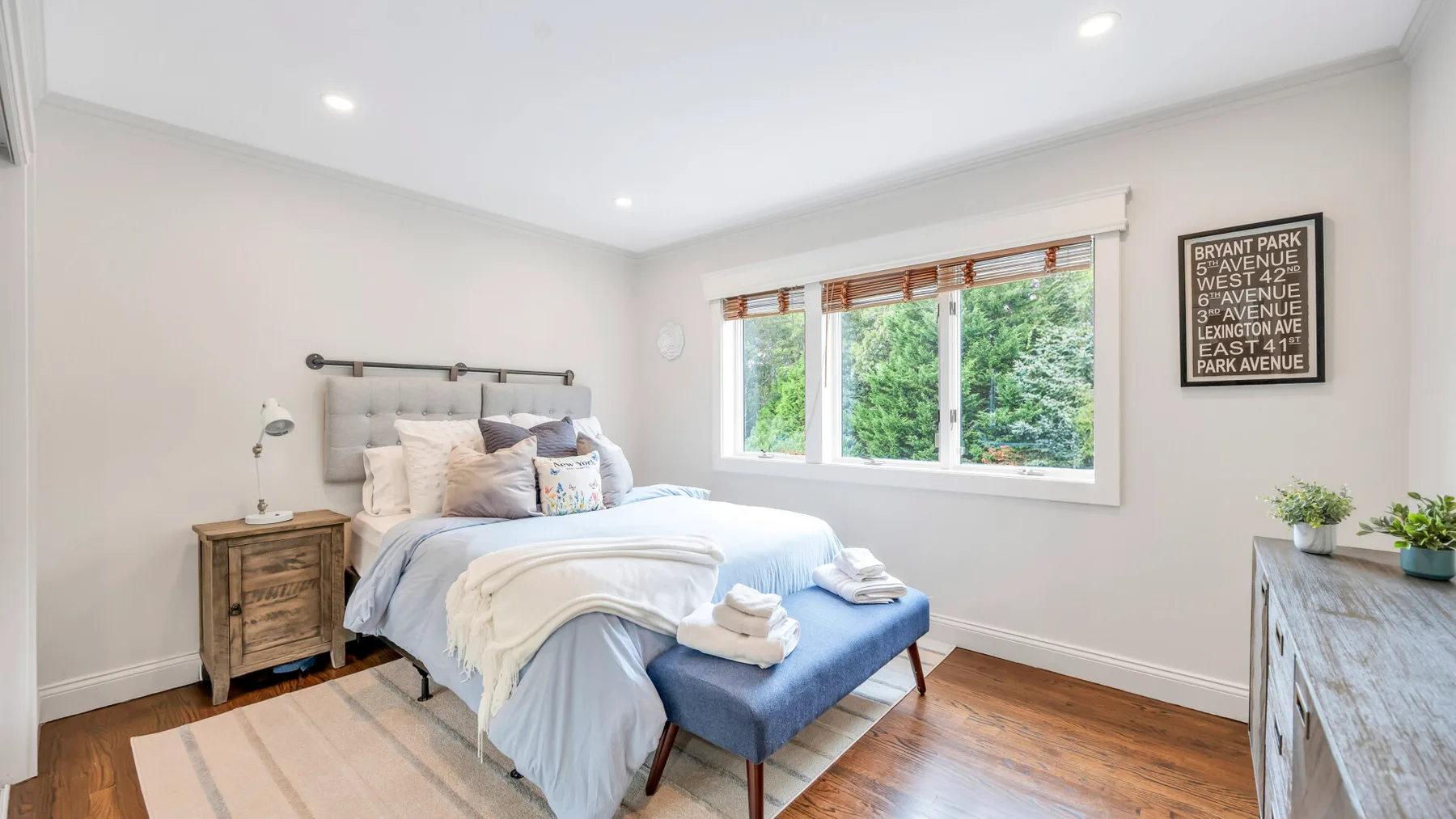 Un dormitorio luminoso con una cama junto a amplias ventanas con vistas a la vegetación.