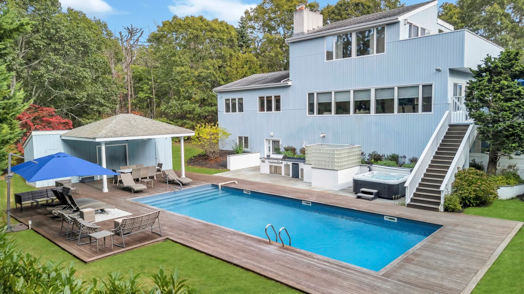 Una piscina y una terraza de madera junto a una casa azul claro.