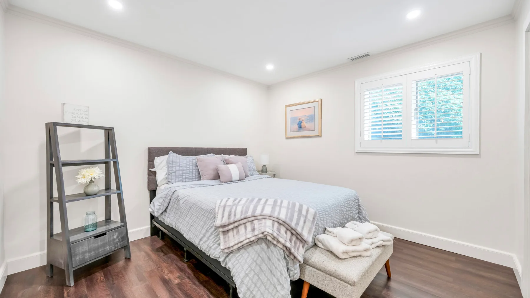 Un dormitorio con una cama, una estantería pequeña y una ventana con persianas.