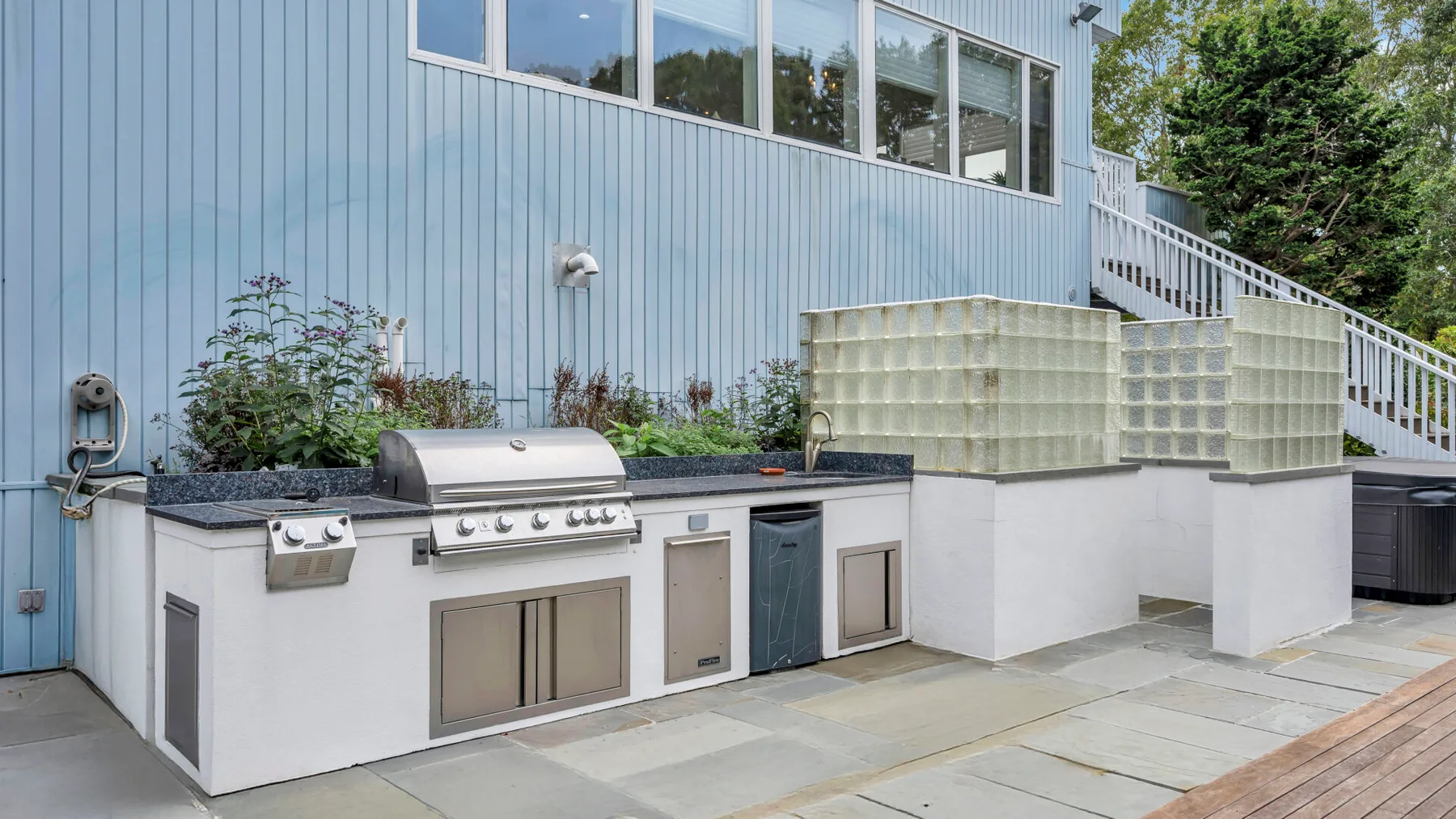 Una cocina exterior con parrilla integrada está junto a un edificio de revestimiento azul.