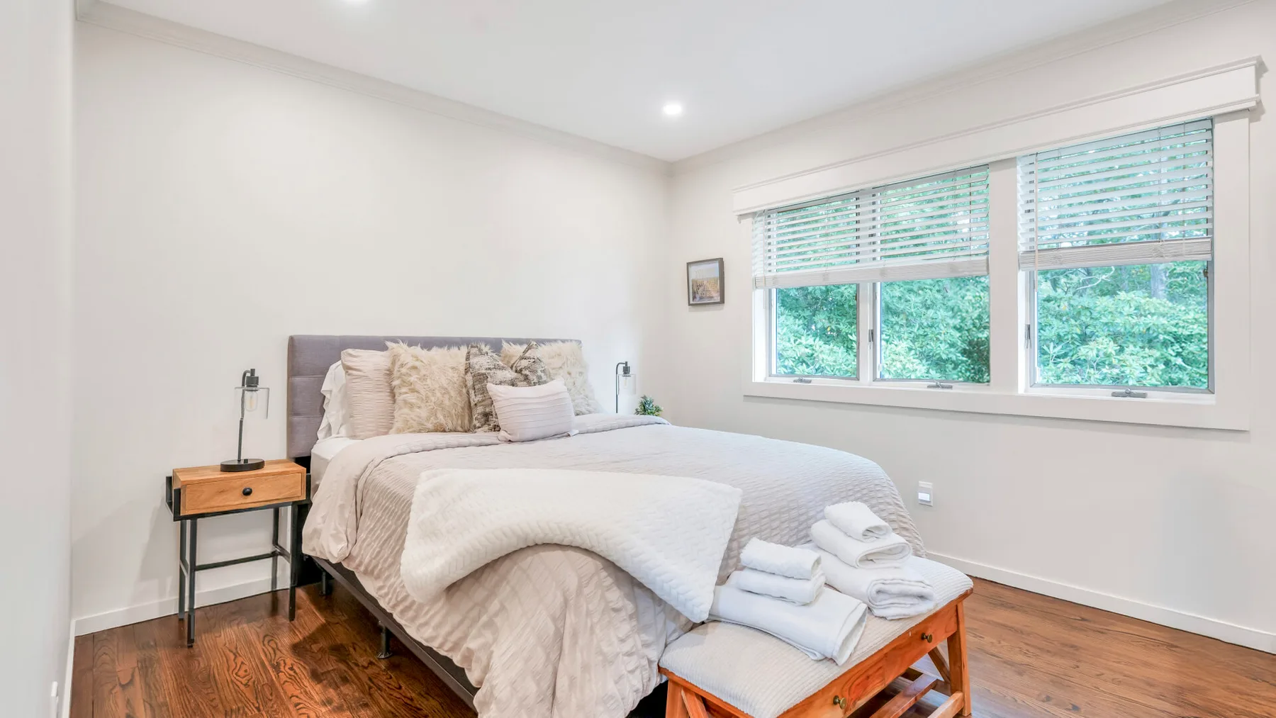 Un dormitorio luminoso con una cama bajo amplias ventanas y toallas dobladas cerca.