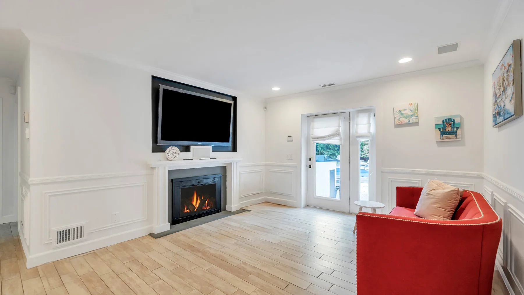 Una sala de estar luminosa con chimenea, televisor en la pared y asientos rojos.