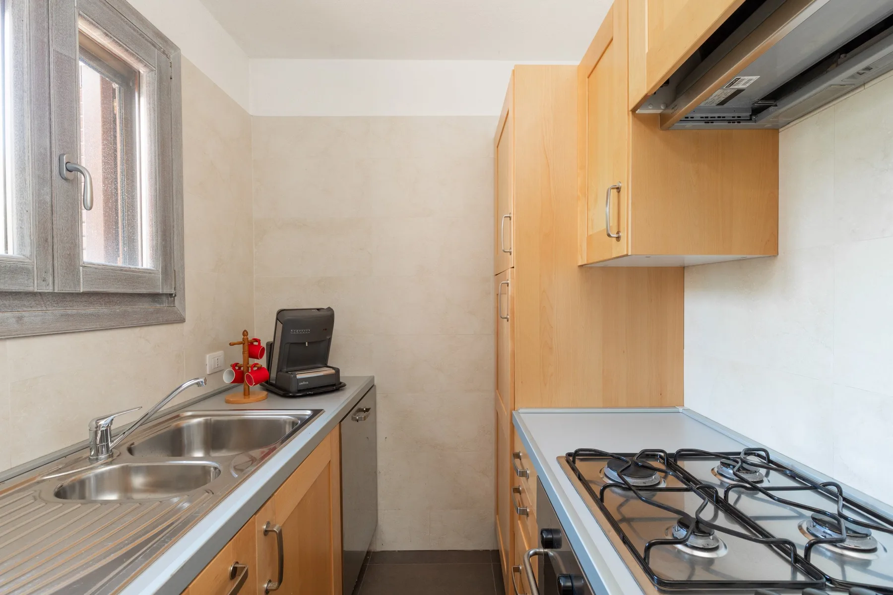 Una cocina compacta con fregadero, cocina de gas y armarios de madera clara.