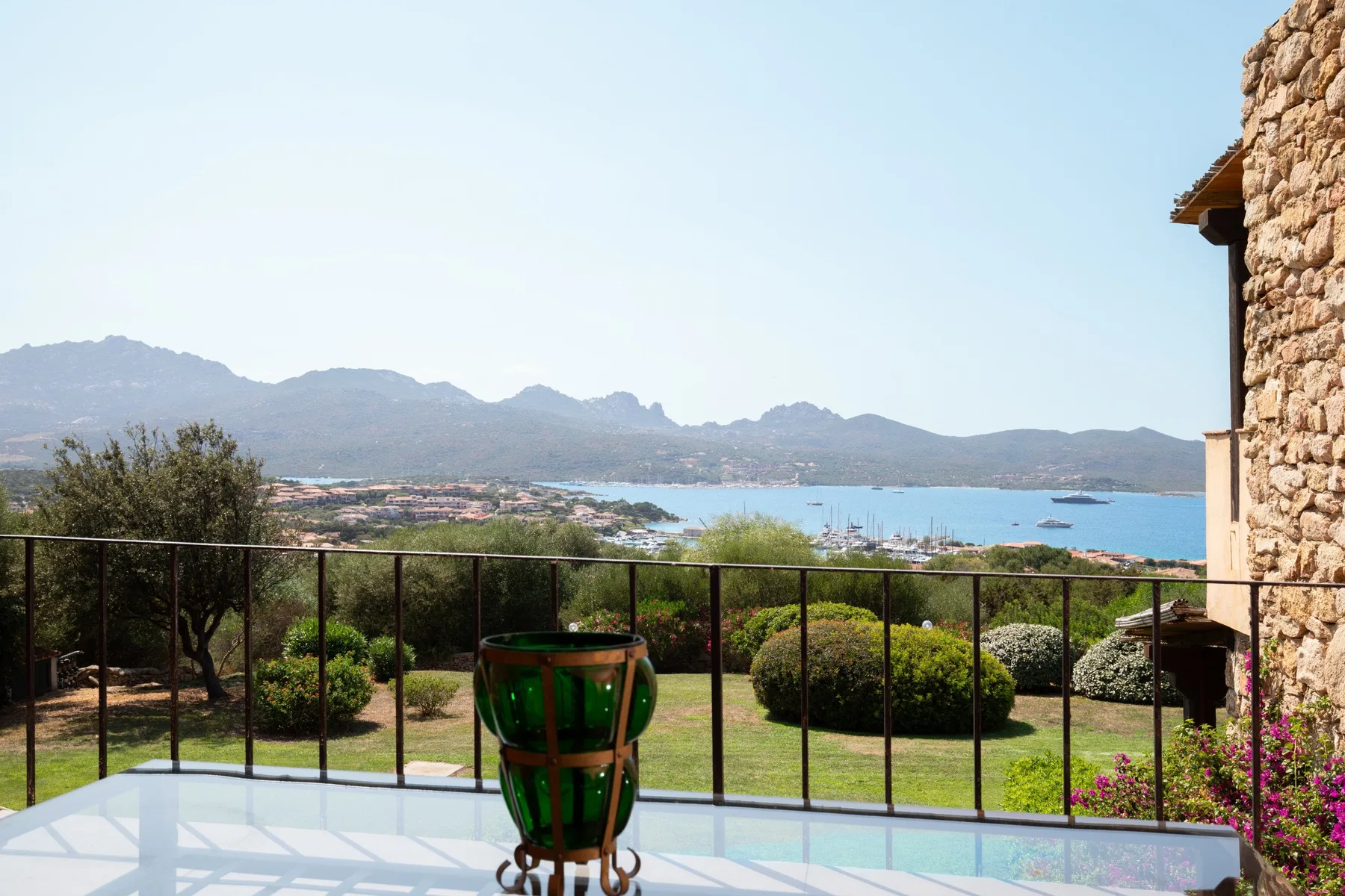 Una terraza da a una bahía, con montañas visibles más allá del jardín.
