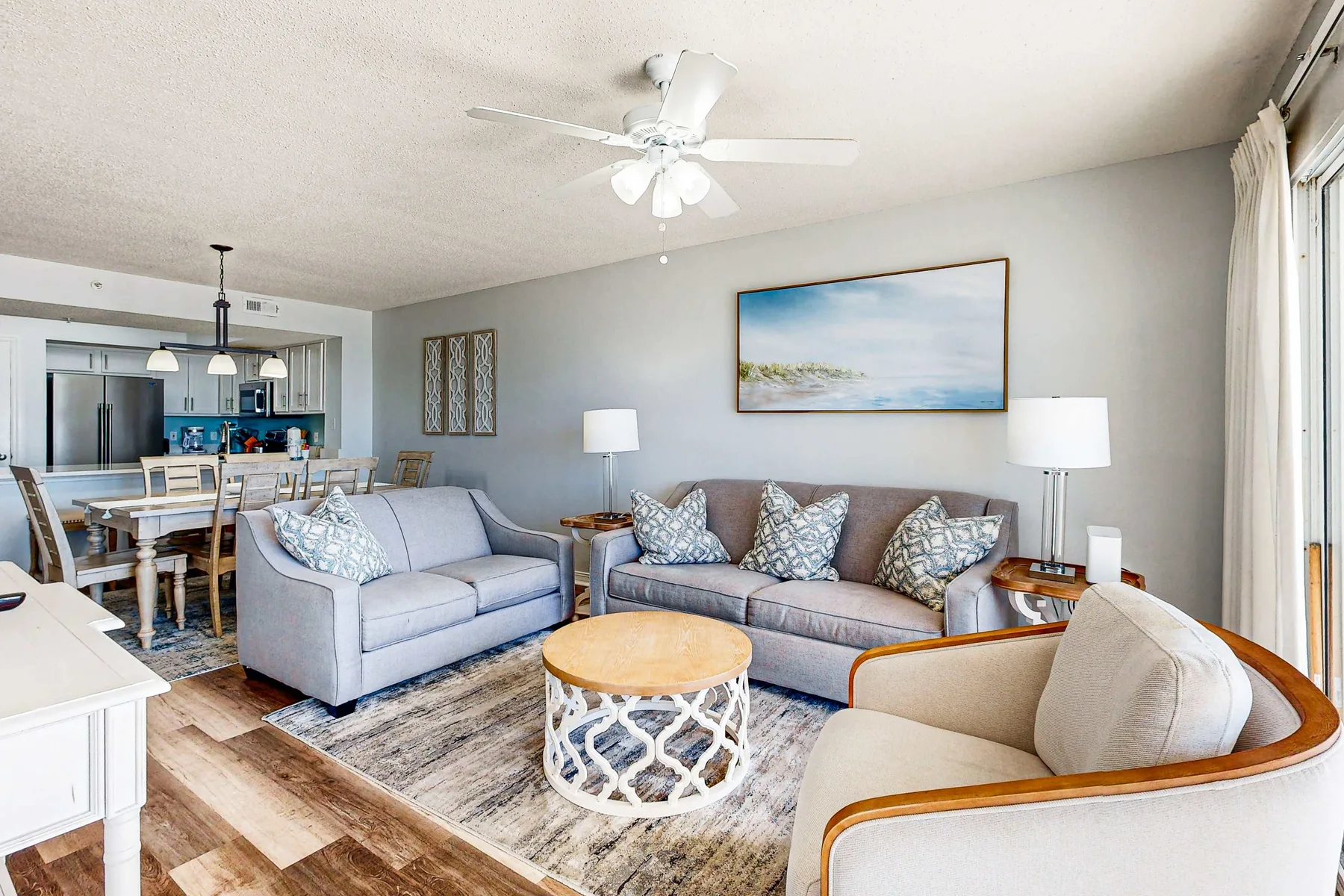 A bright living room with seating around a coffee table, opening onto a dining area.