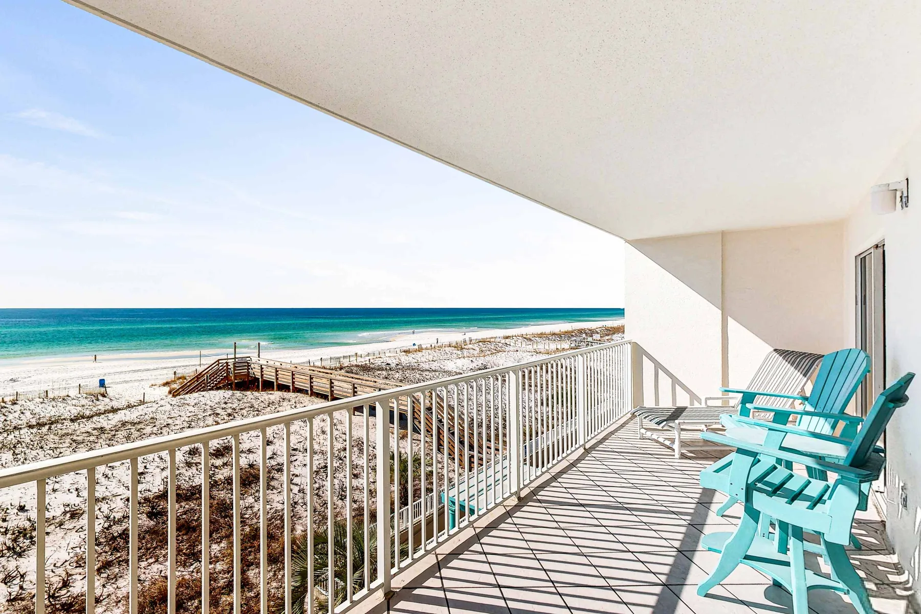 A covered balcony overlooks the beach and ocean, with turquoise seating along the railing.