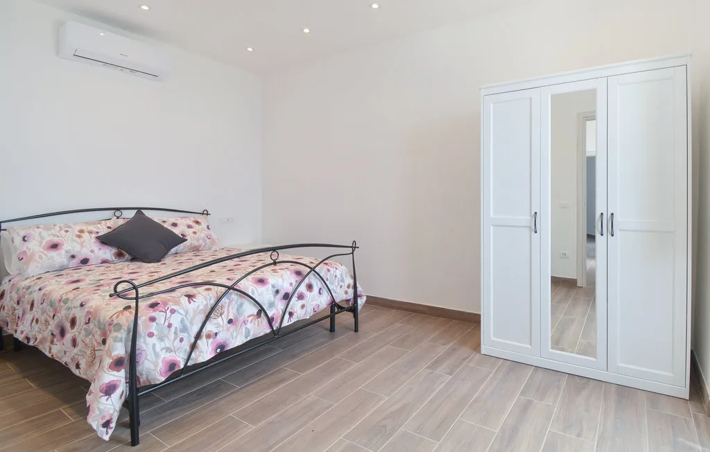 A bright bedroom with a floral bedspread and a white wardrobe.