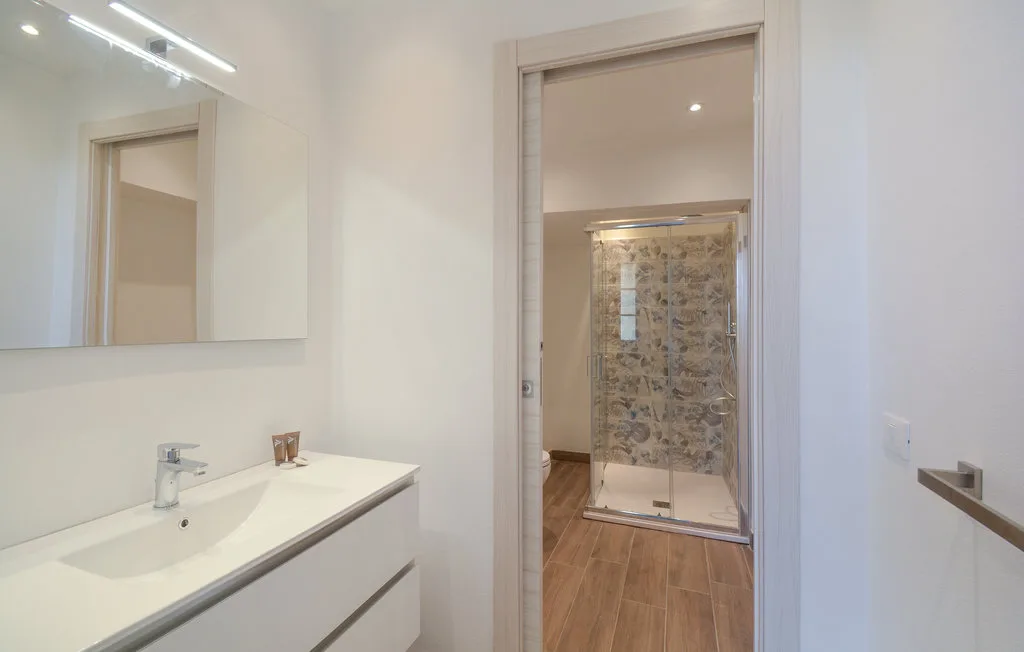 A bright bathroom with a white sink and a shower in the adjoining space.