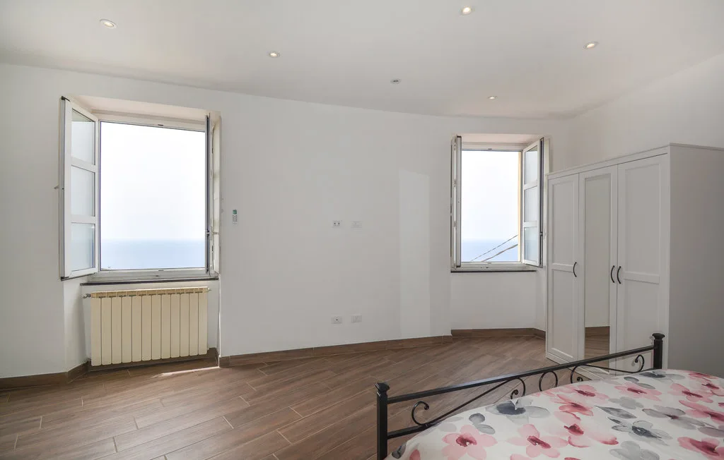A bright bedroom with two open windows and a bed with floral bedding.