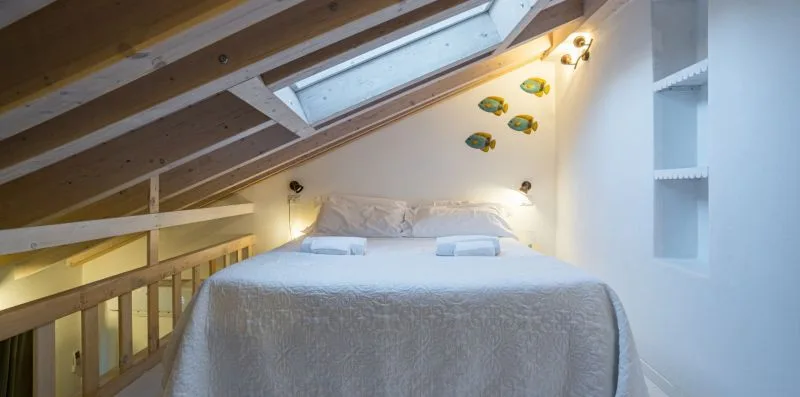 A bedroom with a bed beneath a sloped ceiling and skylight.
