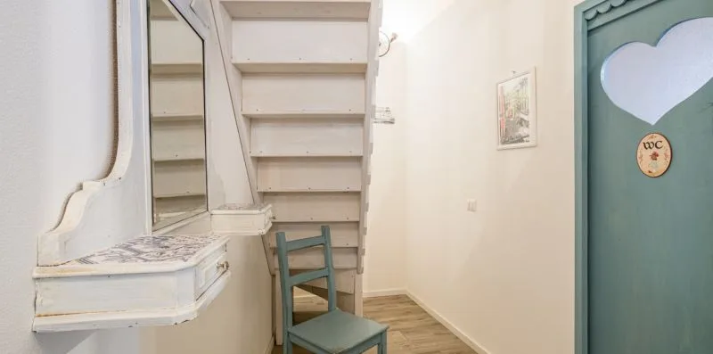 A narrow indoor hallway with a wooden chair beside a staircase.