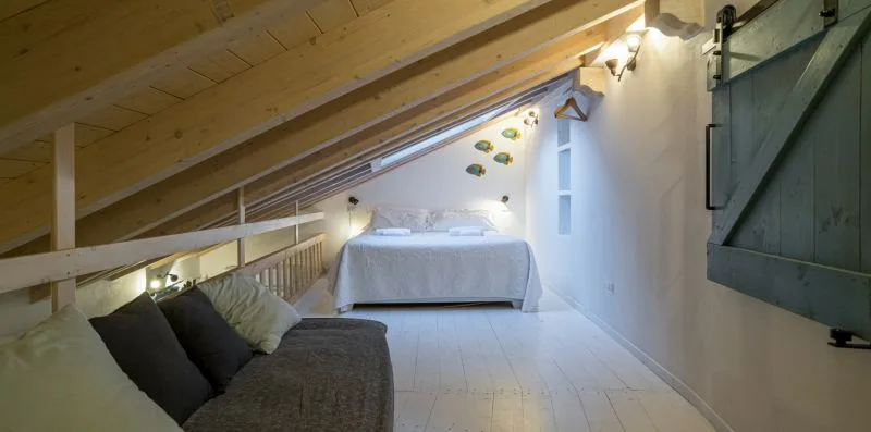 A bedroom under a sloped wooden ceiling, with a bed and seating.