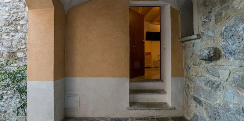 A stone passage leads to an open doorway and a warmly lit room.
