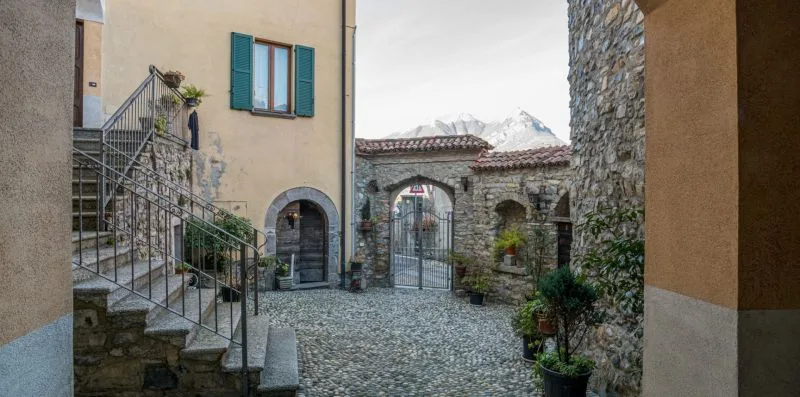 Un patio de piedra con un arco enrejado y montañas al fondo.