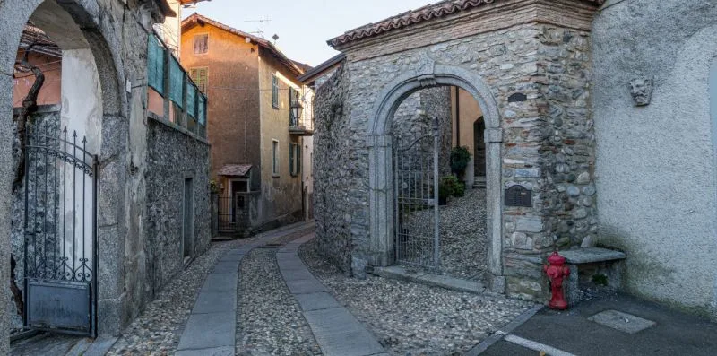 Un callejón empedrado pasa junto a un arco de piedra y edificios cercanos.