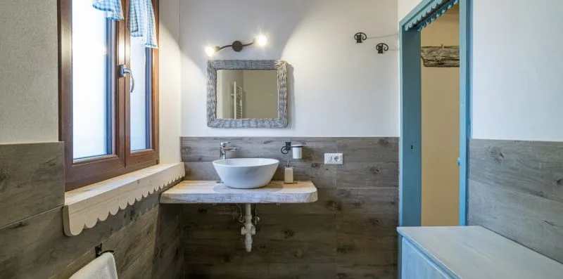 A bathroom vanity with a vessel sink sits beside a window.