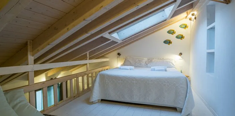 Una cama está bajo un techo inclinado de madera con tragaluces.