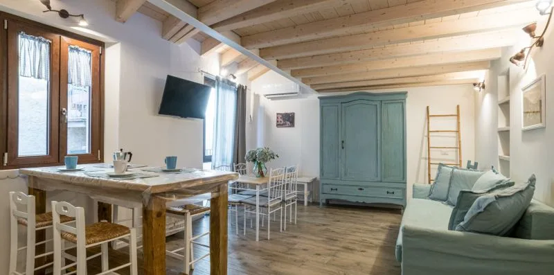 Zona de comedor y estar con una mesa de madera, sillas y un sofá verde.