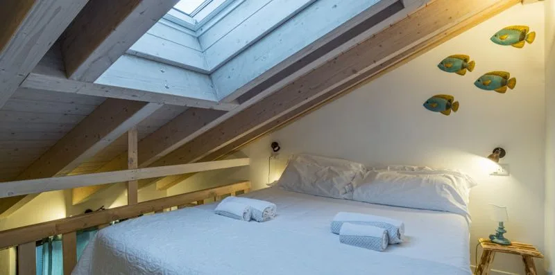 A bedroom with a bed beneath a sloped ceiling and skylight.