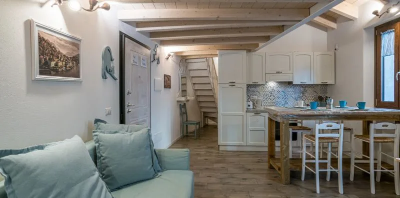 A bright open-plan room with seating, a kitchen counter, and stairs.