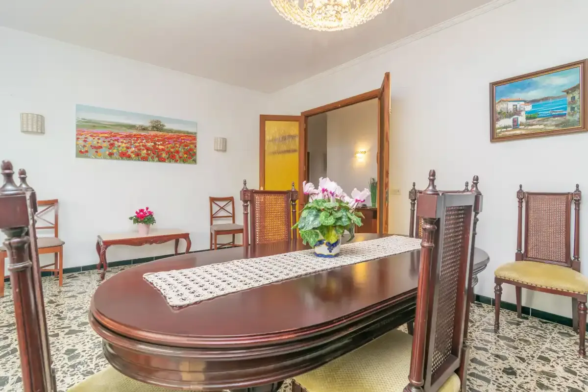 Dining room with a long table, chairs, and colorful paintings on the walls.