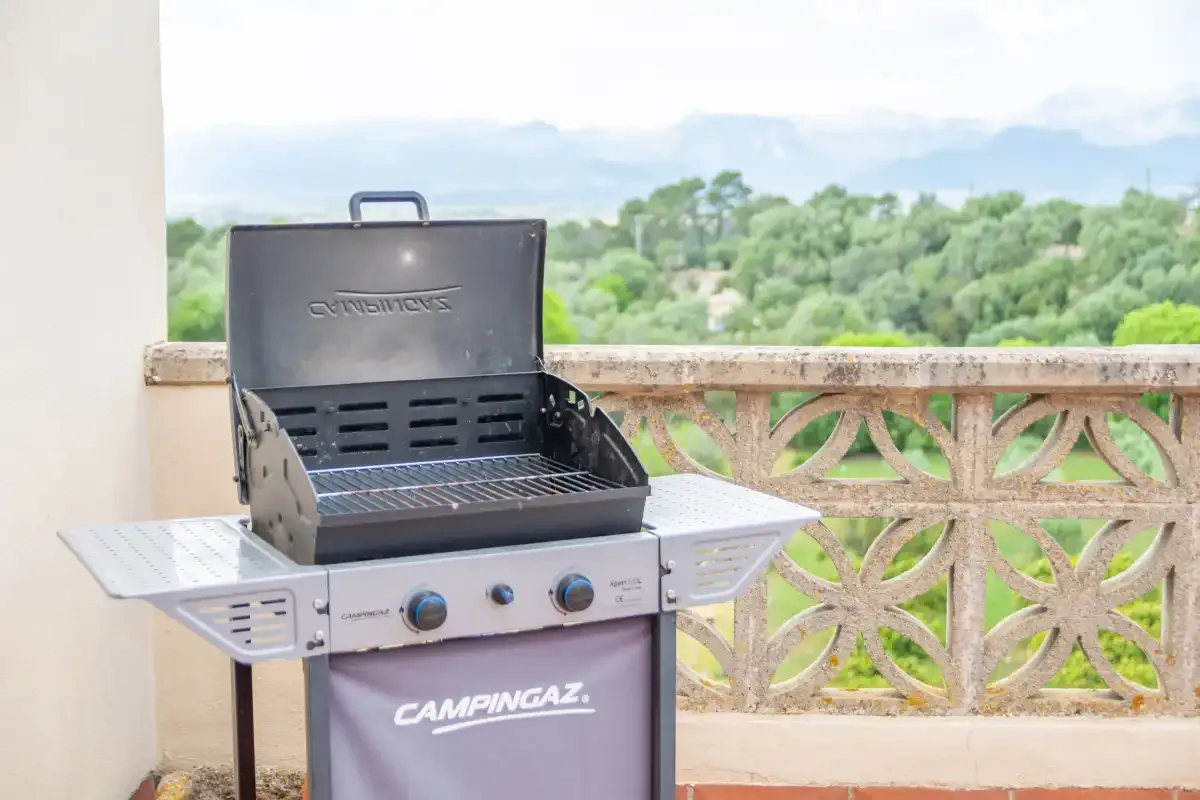 A barbecue grill stands on a balcony overlooking green trees.