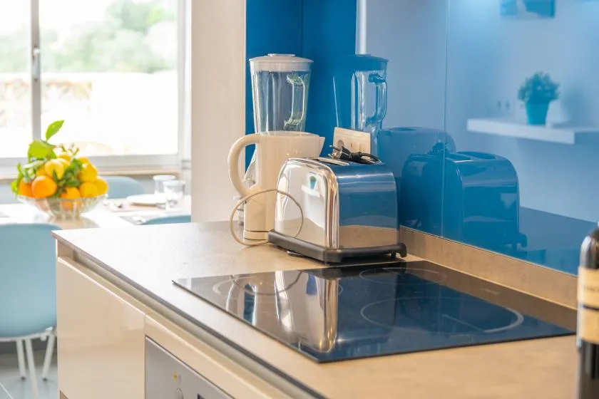 A bright kitchen counter holds small appliances beside a glass cooktop.