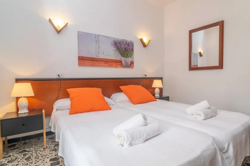 A bedroom with two beds, orange pillows, and wall lighting.