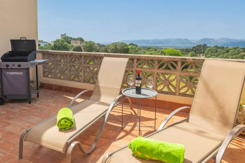 A sunny terrace with reclining loungers, a small table, and a view of distant hills.