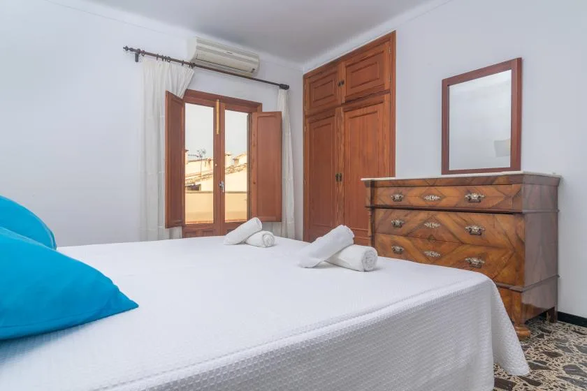 A bedroom with a bed, wooden wardrobe, and dresser beside a window.