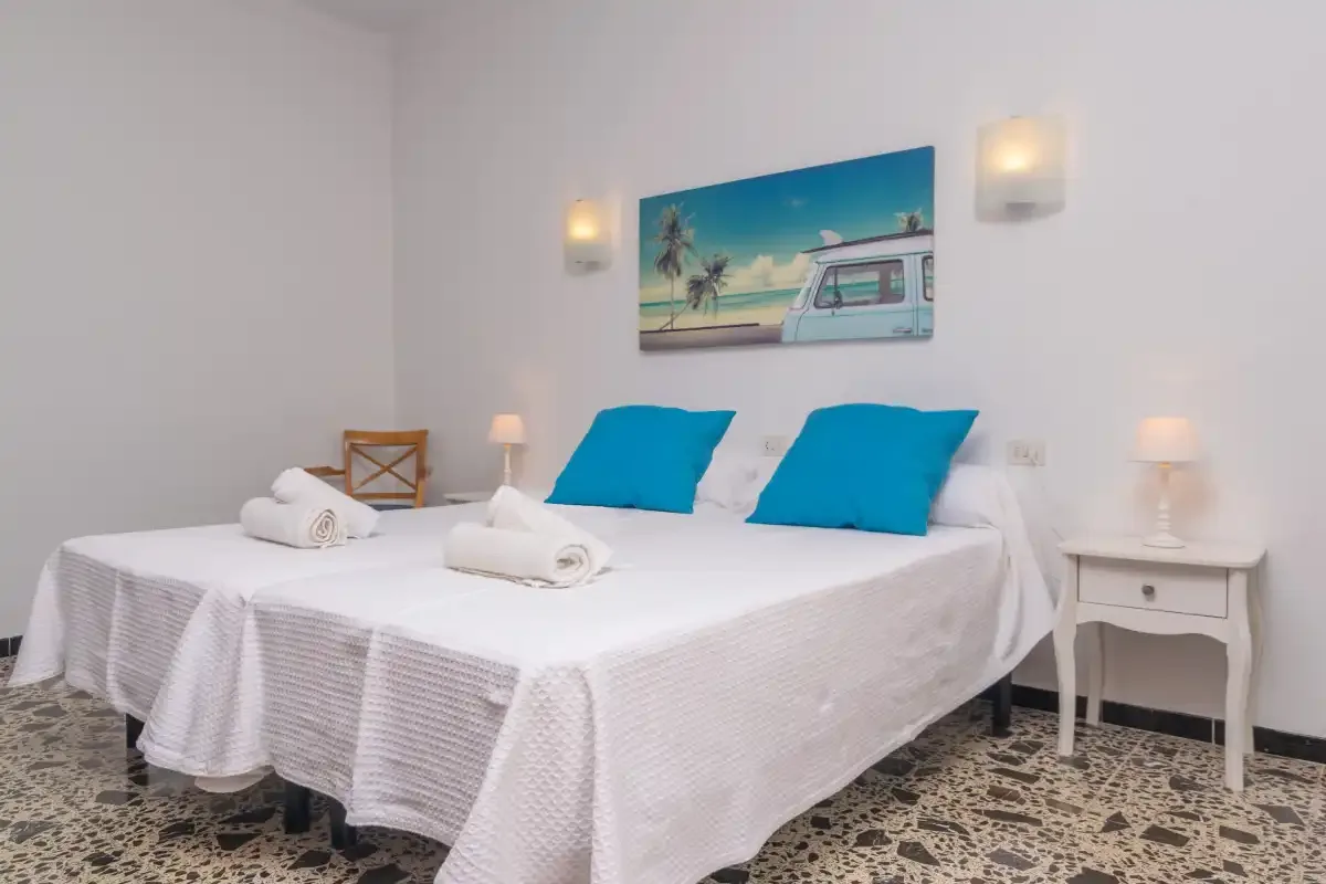 A bedroom with two beds, turquoise pillows, and beach-themed wall art.
