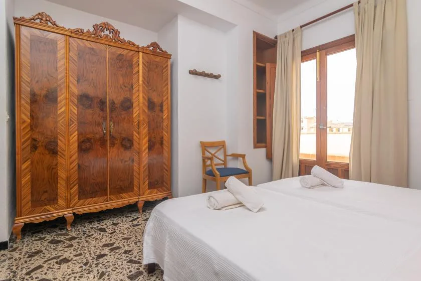 A bedroom with a large wooden wardrobe beside a bed and bright window.