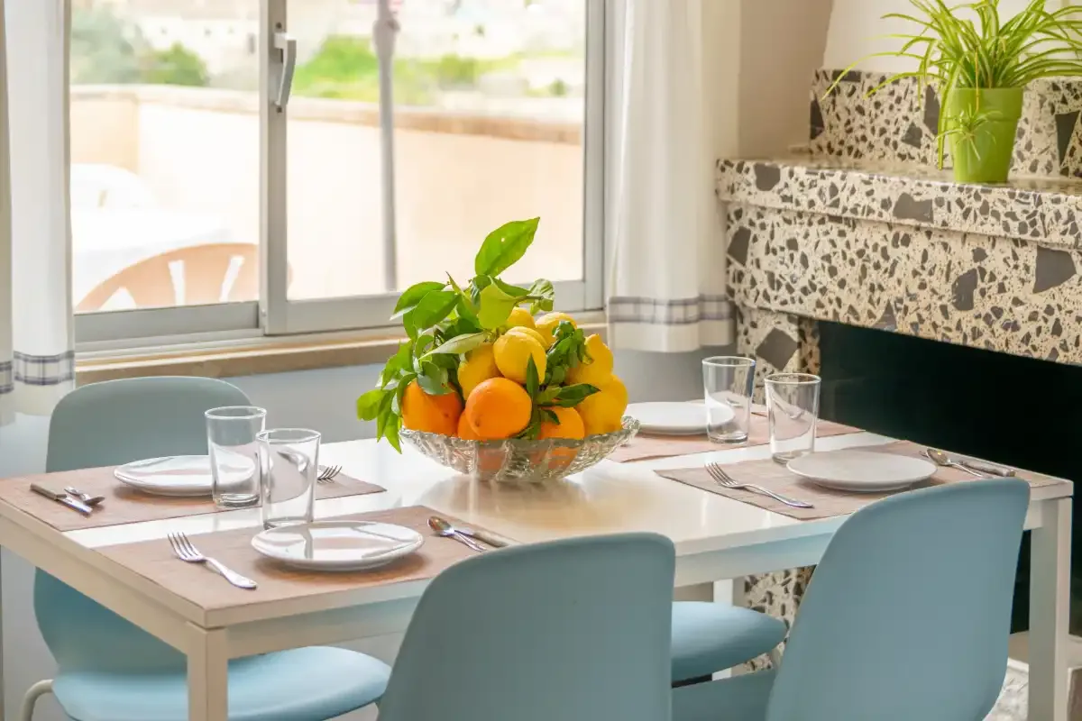 A dining area with a set table and a bowl of fruit.