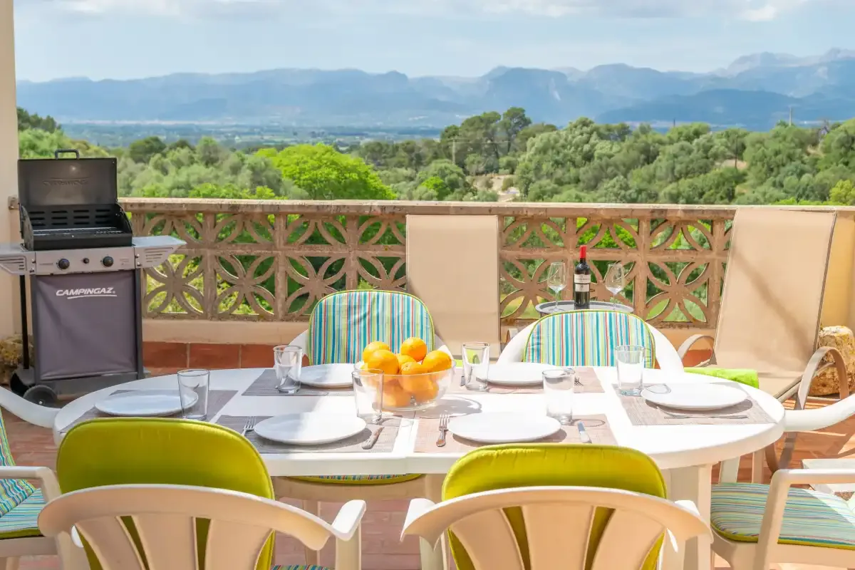An outdoor dining area with a table and chairs overlooks green hills and distant mountains.
