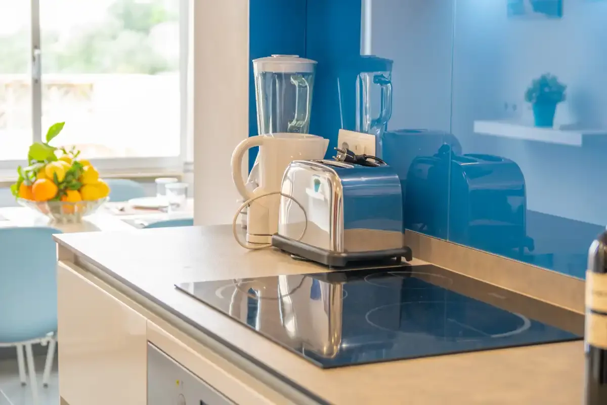 A bright kitchen counter holds a toaster and blender beside a cooktop.