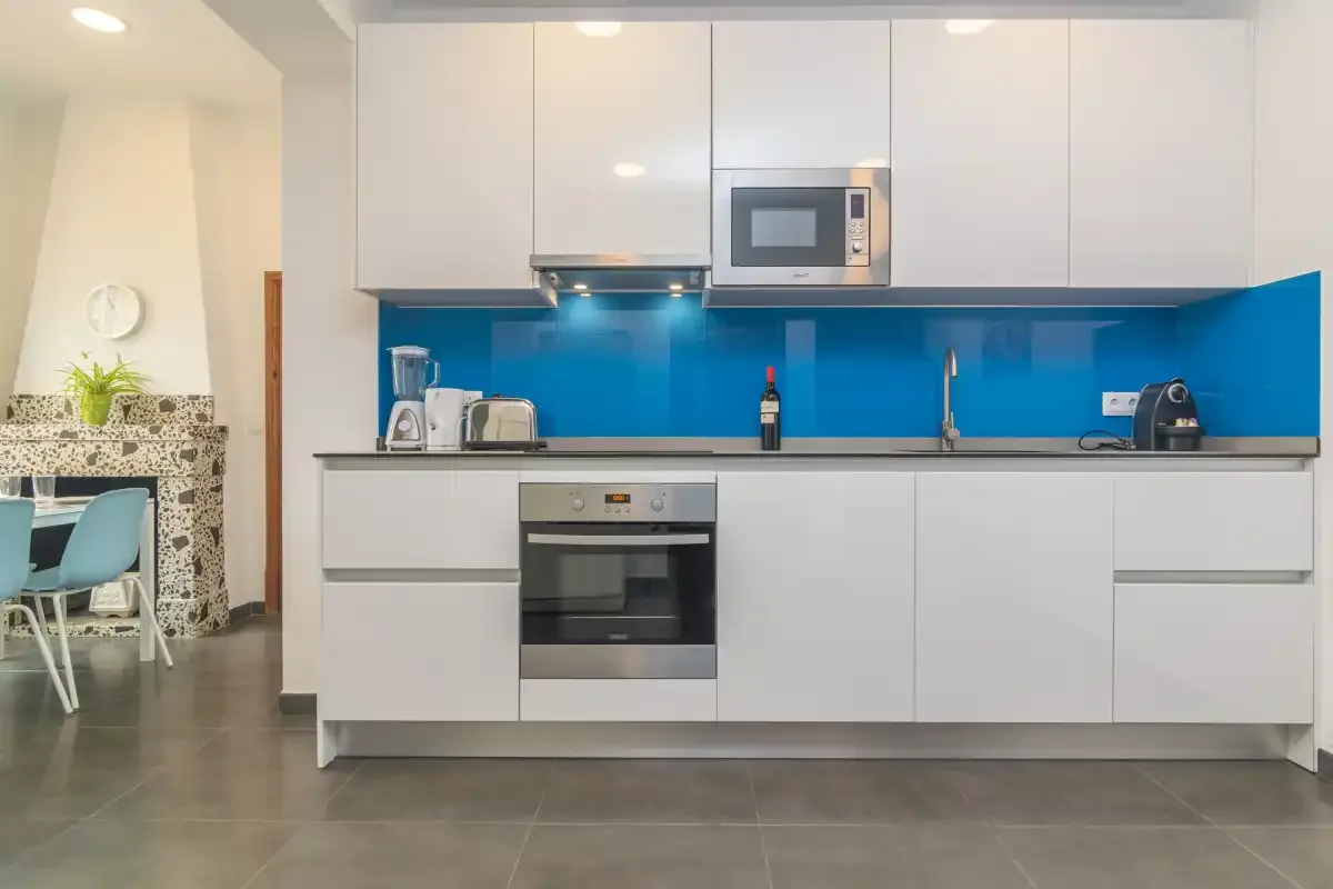 A modern kitchen with white cabinets and a bright blue backsplash.