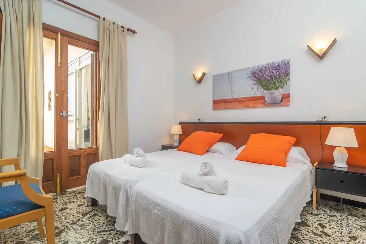 A bedroom with a double bed, orange cushions, and a framed floral picture.