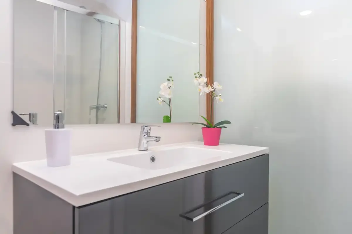 A bathroom vanity with a wide mirror and a small potted orchid.