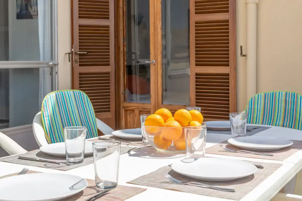 A patio dining table is set with plates and a bowl of oranges.