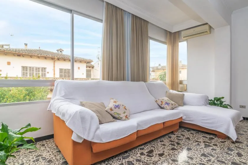 A bright living room with white-covered seating beside large windows and curtains.