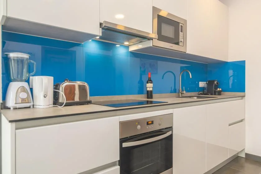 A modern kitchen with white cabinets, blue backsplash, and built-in appliances.
