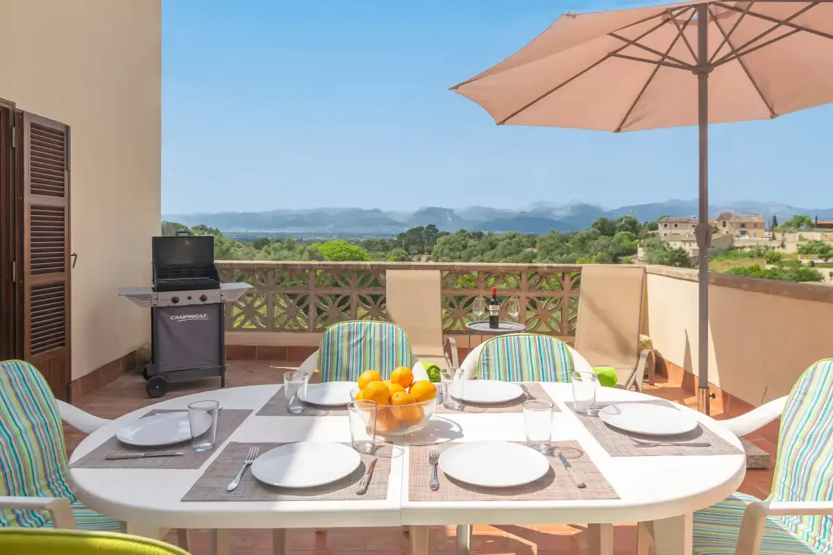A terrace dining area overlooks a green landscape beneath a large umbrella.