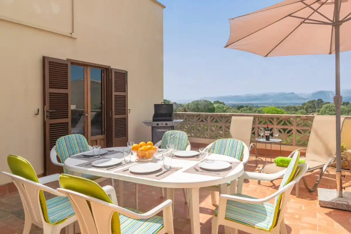 A sunny terrace dining area with outdoor seating and a view of distant hills.