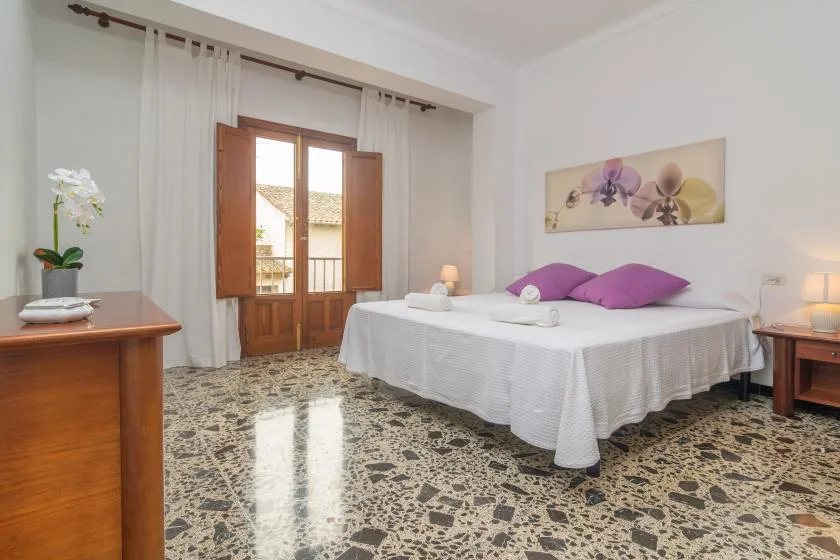 A bright bedroom with a double bed, purple pillows, and wooden shutters.