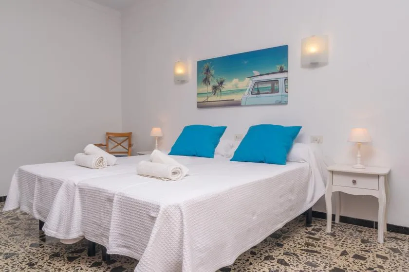 A bright bedroom with two beds, white linens, and blue pillows.