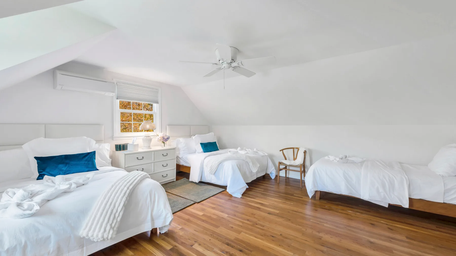 A bright bedroom with several beds, white bedding, and a ceiling fan.
