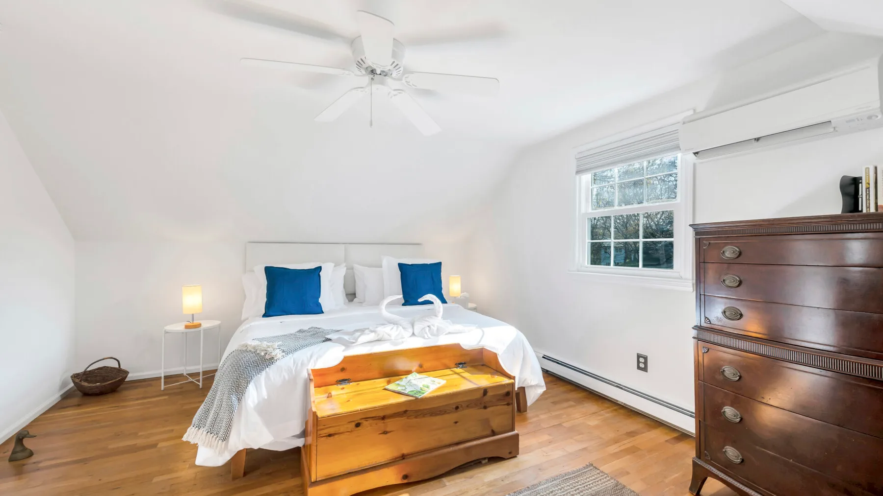 A bright bedroom with a bed, wooden chest, and window.