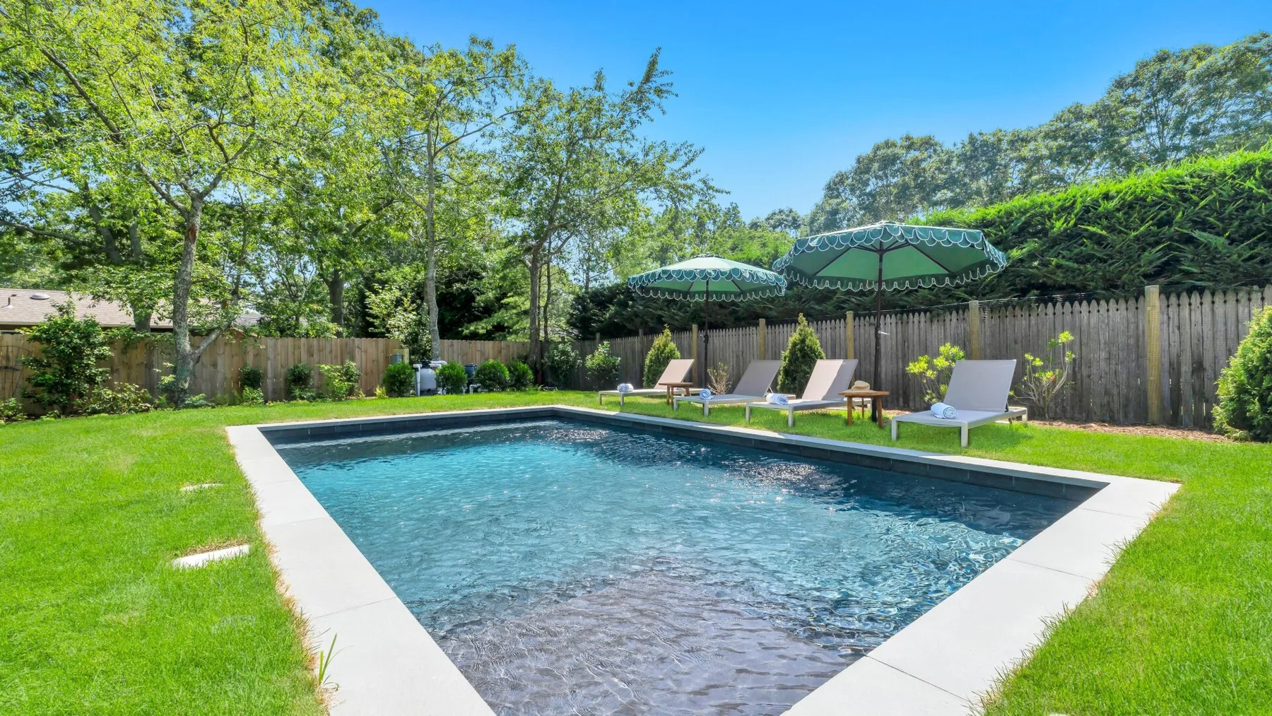 An outdoor swimming pool sits in a grassy yard beneath shaded seating.