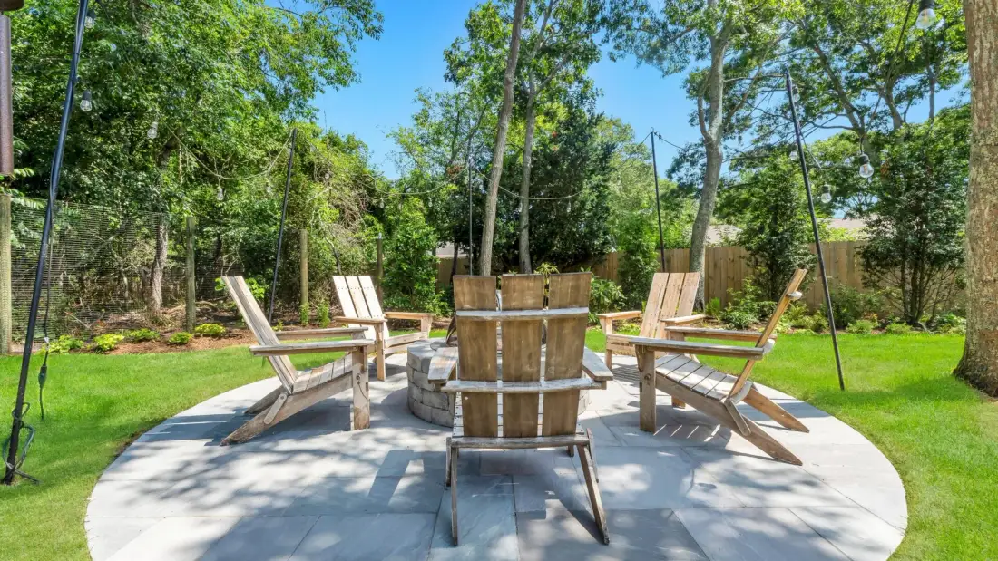 An outdoor seating area on a paved patio is surrounded by trees and greenery.