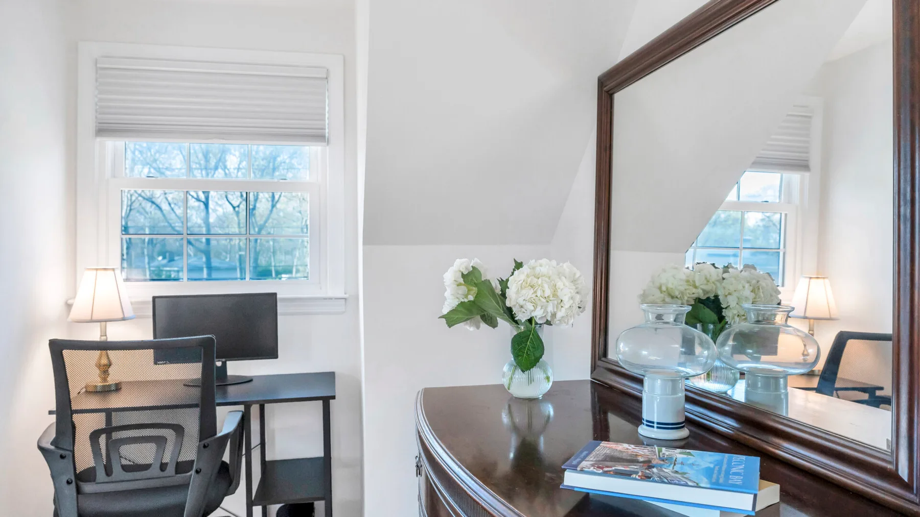 A desk and computer sit beside a window with a partially lowered blind.